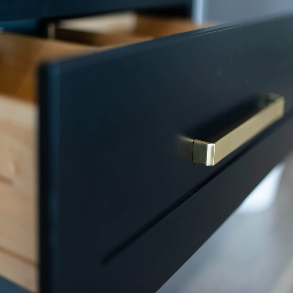 Close-up of a black kitchen drawer with a gold handle.
