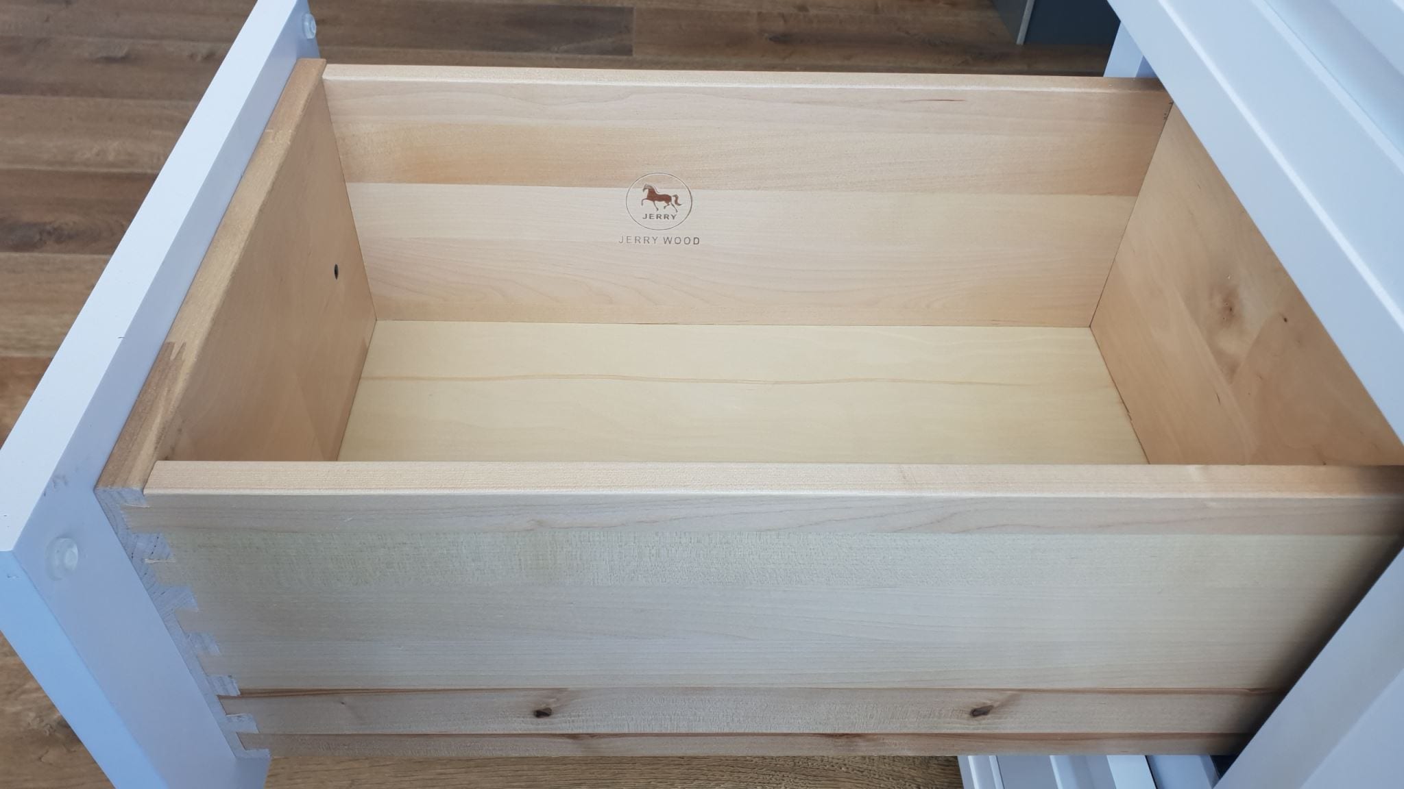 Wooden kitchen drawer with light finish, open and empty.