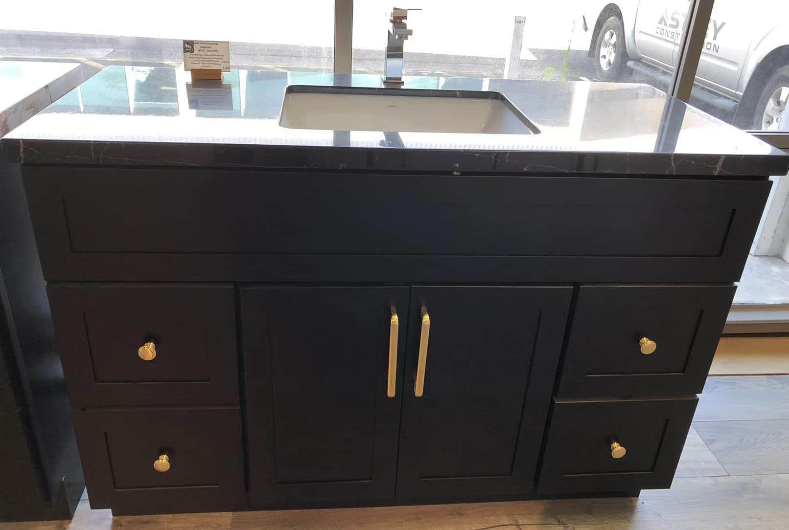 Black kitchen cabinet with sink and gold handles.