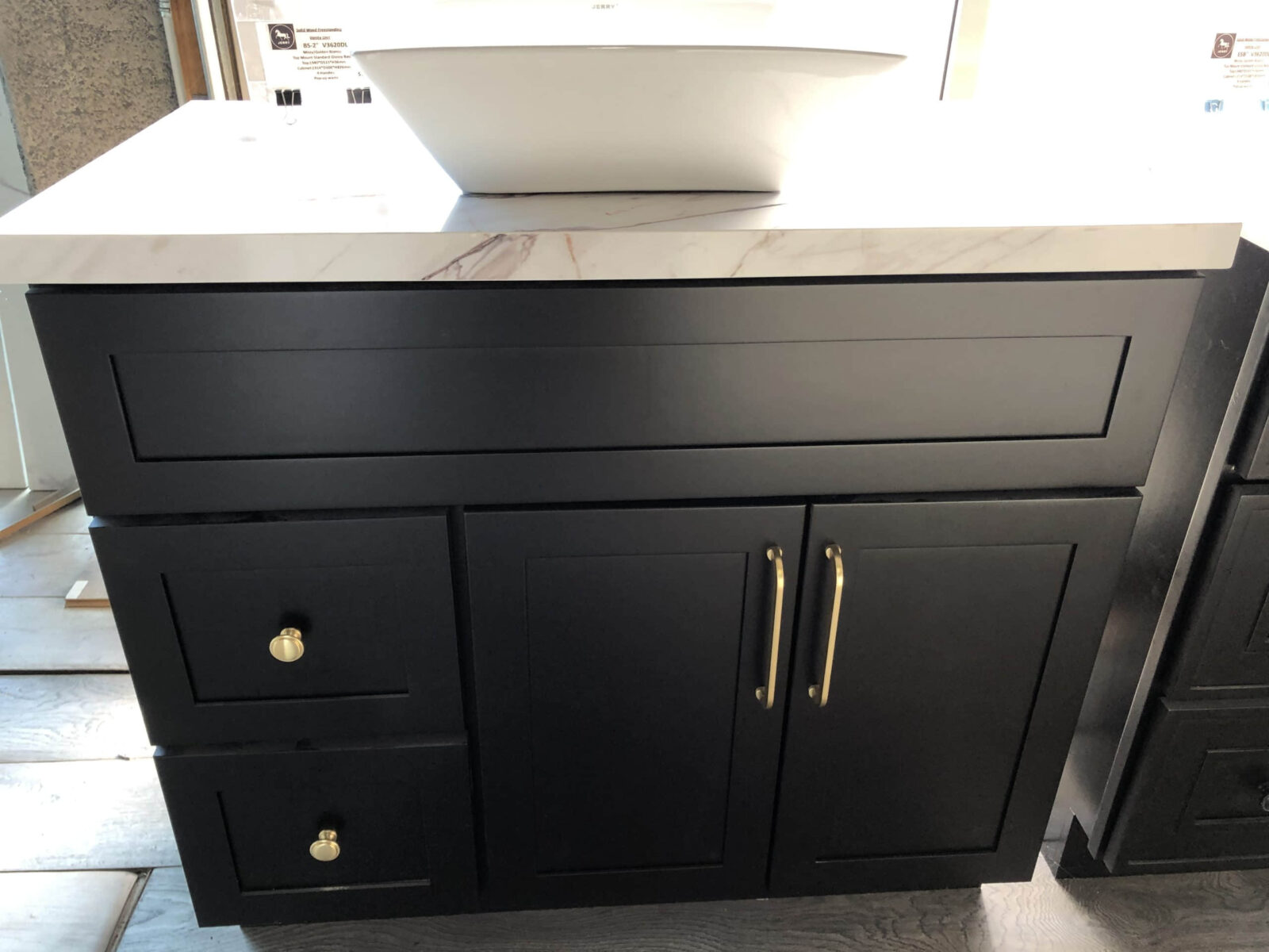 20220317152115-scaled-1.jpg Black kitchen cabinet with marble countertop and white sink.