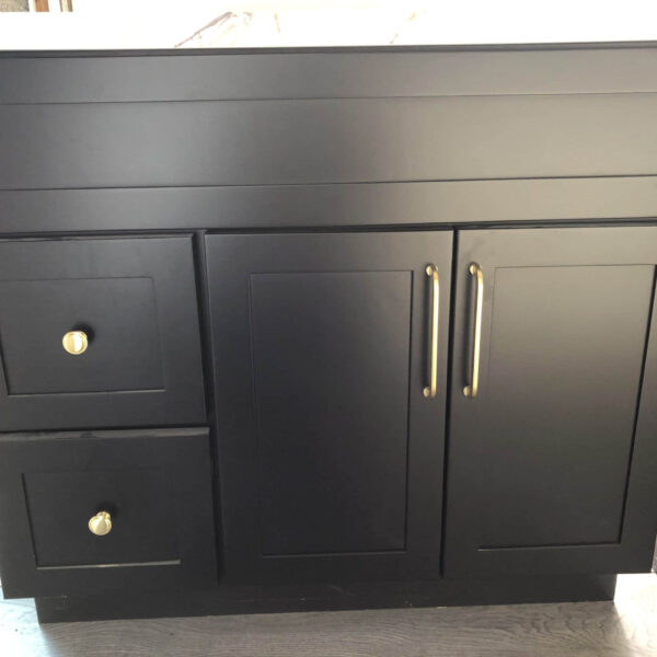 Black kitchen cabinet with gold handles and drawers.