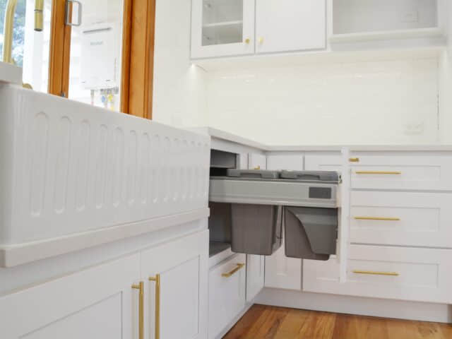 An example of a clean white modern kitchen with a butler sink and gold brass handles.