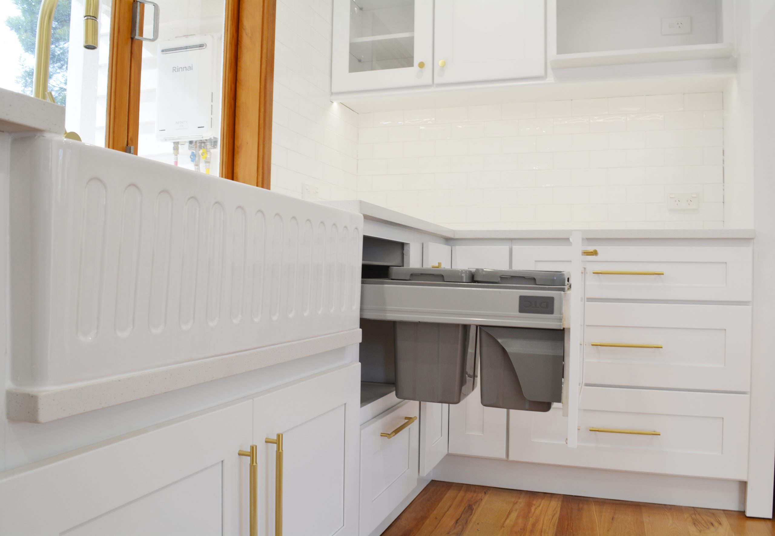 An example of a clean white modern kitchen with a butler sink and gold brass handles.