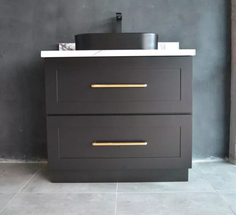 Black freestanding vanity with gold handles against dark wall.