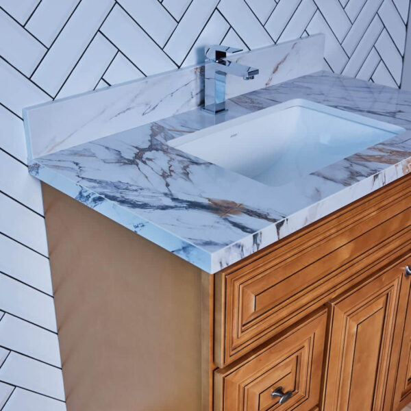 Marble countertop with sink and wooden cabinet against herringbone tile wall.
