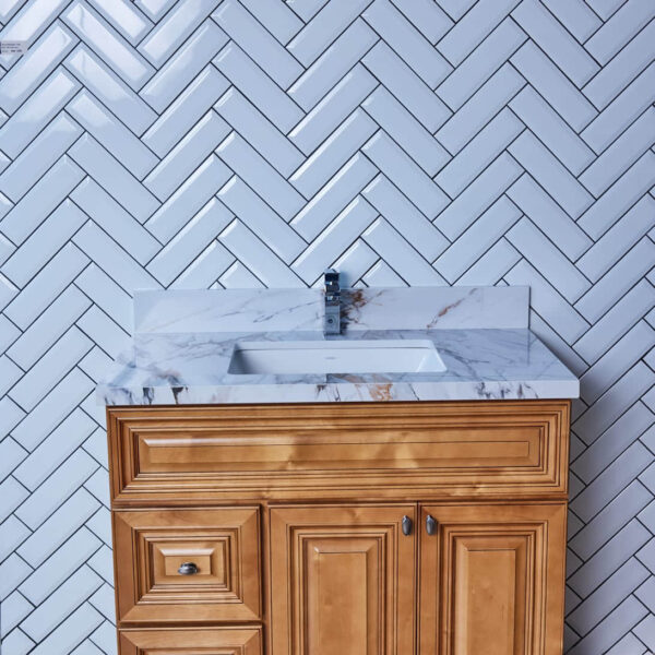 Wooden bathroom vanity with marble countertop and herringbone tile backsplash.