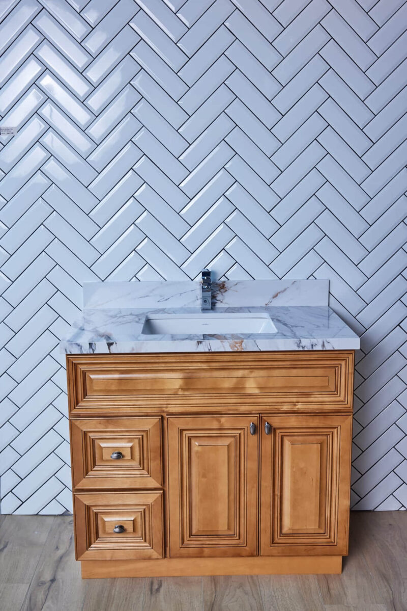 Wooden bathroom vanity with marble countertop and herringbone tile backsplash.