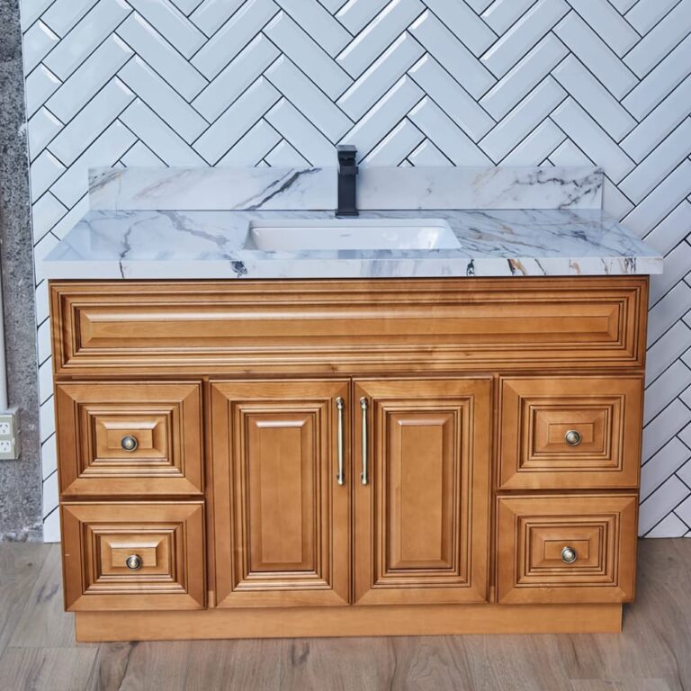 Wooden bathroom vanity with marble countertop against herringbone tile wall.