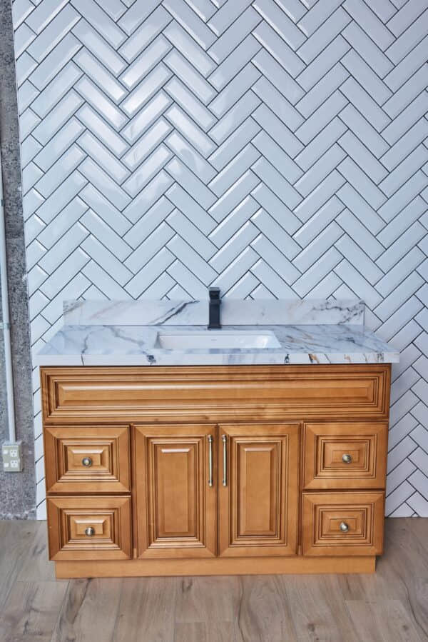 Wooden bathroom vanity with marble countertop against herringbone tile wall.
