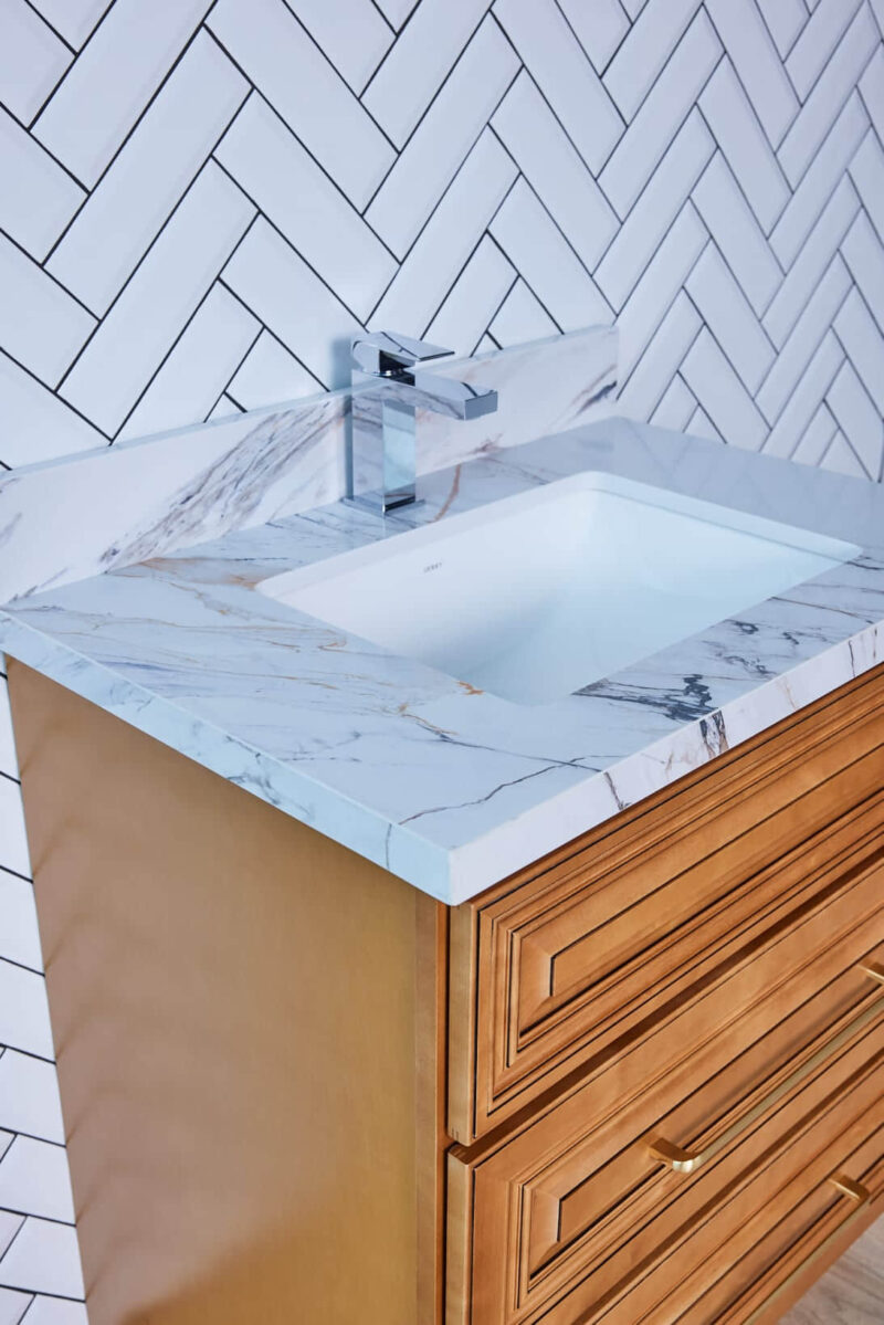 Marble countertop with sink and wooden cabinet against herringbone tile wall.