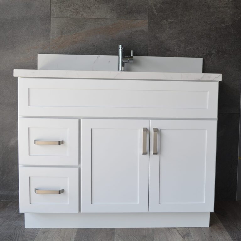 White bathroom vanity with drawers and sink against dark tiled wall.