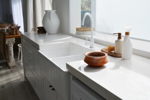 Modern kitchen with white countertops, sink, and decorative items near a window.