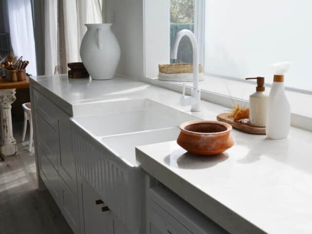 Modern kitchen with white countertops, sink, and decorative items near a window.