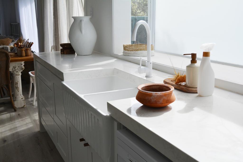 Modern kitchen with white countertops, sink, and decorative items near a window.