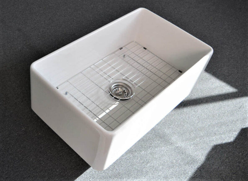 White kitchen sink with metal grid on dark countertop.
