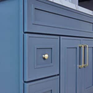 Blue kitchen cabinet with gold handles and marble countertop.