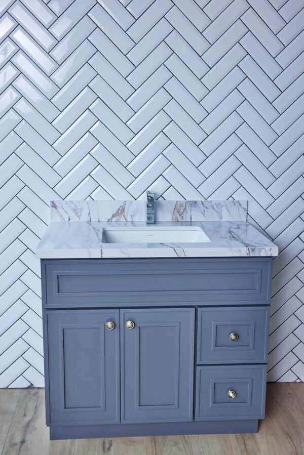 Blue bathroom vanity with marble countertop and herringbone tile backsplash.
