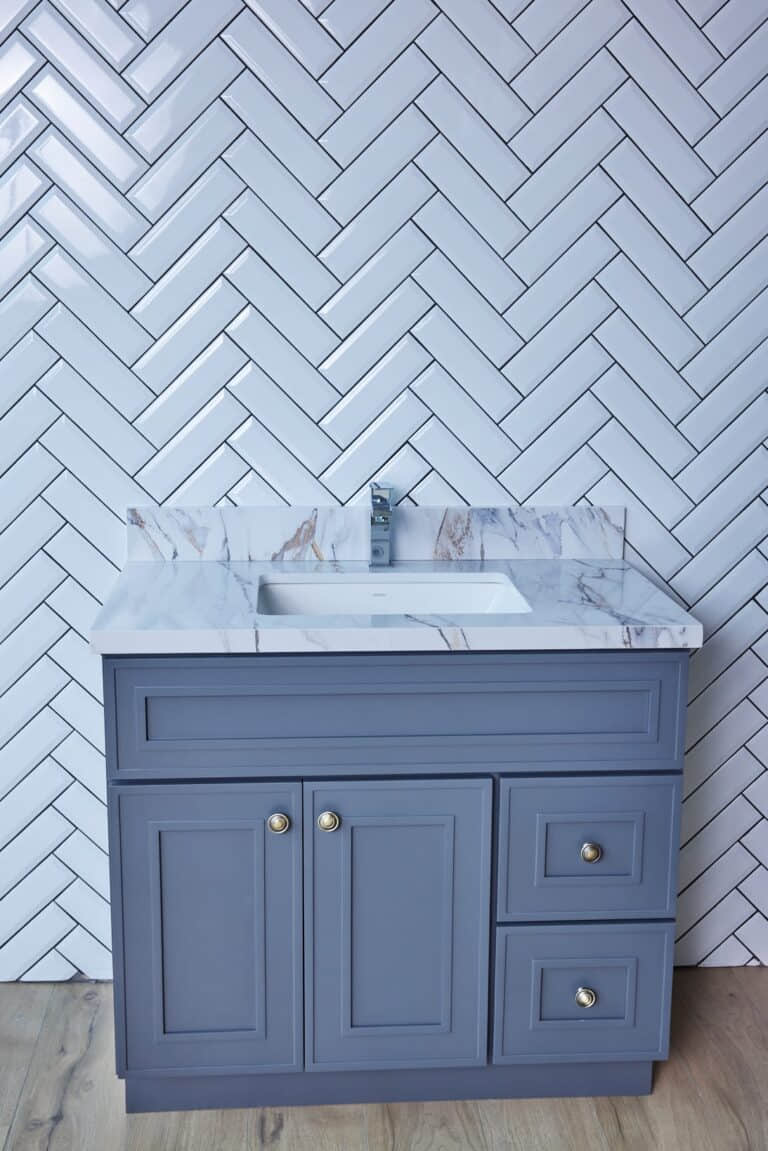 Blue bathroom vanity with marble countertop and herringbone tile backsplash.