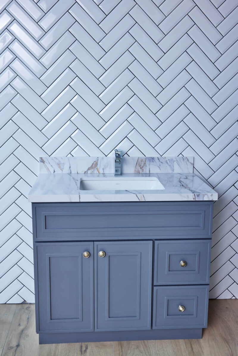Blue bathroom vanity with marble countertop and herringbone tile backsplash.