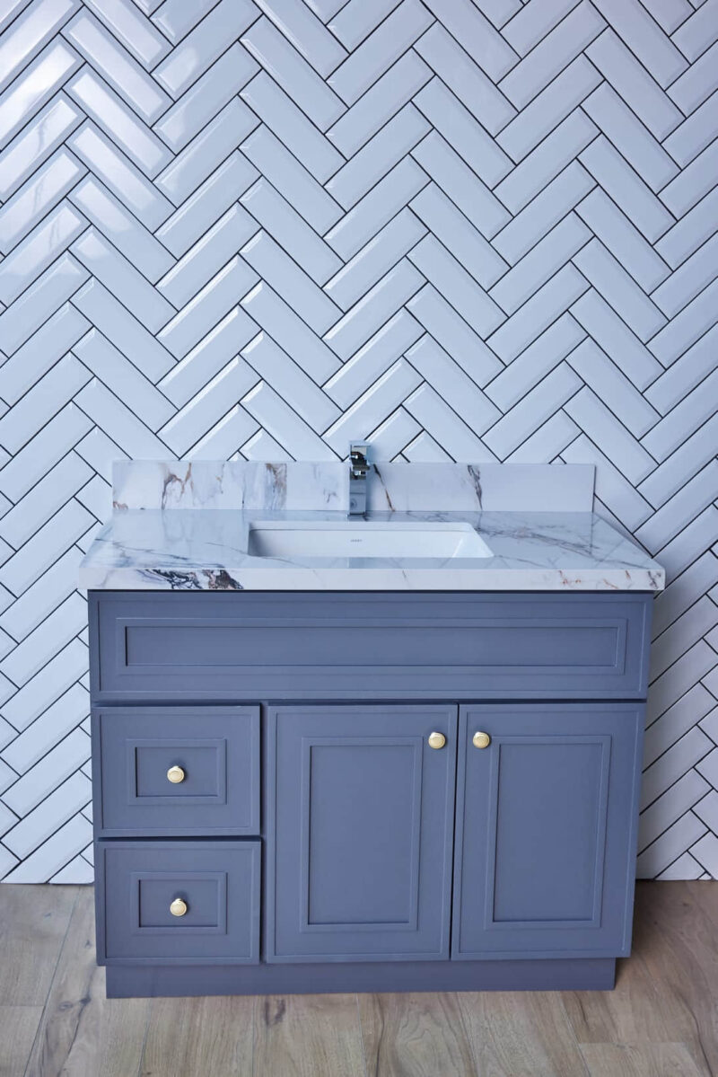 Blue bathroom vanity with marble countertop and herringbone tile backsplash.