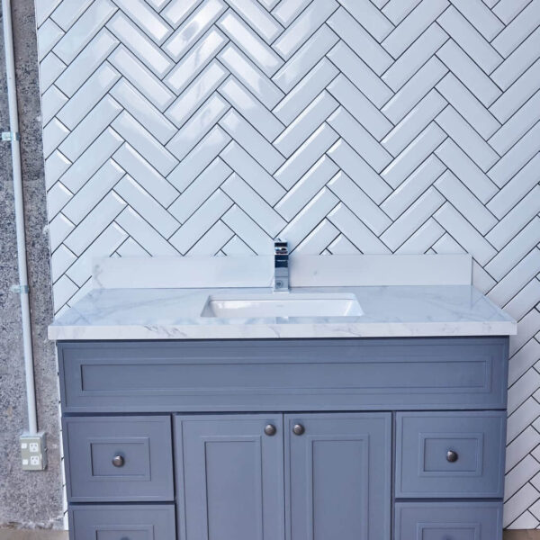 Gray bathroom vanity with marble countertop and herringbone tile backsplash.
