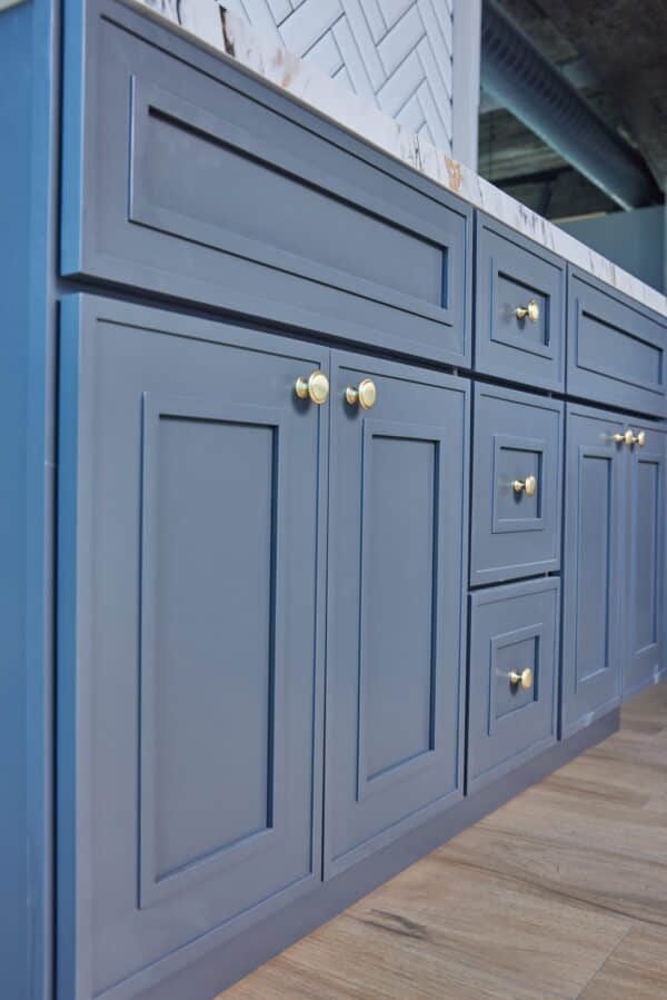 Blue kitchen cabinets with gold handles and marble countertop.