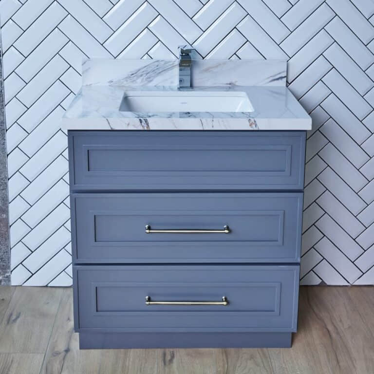 Gray bathroom vanity with marble countertop and herringbone tile backsplash.