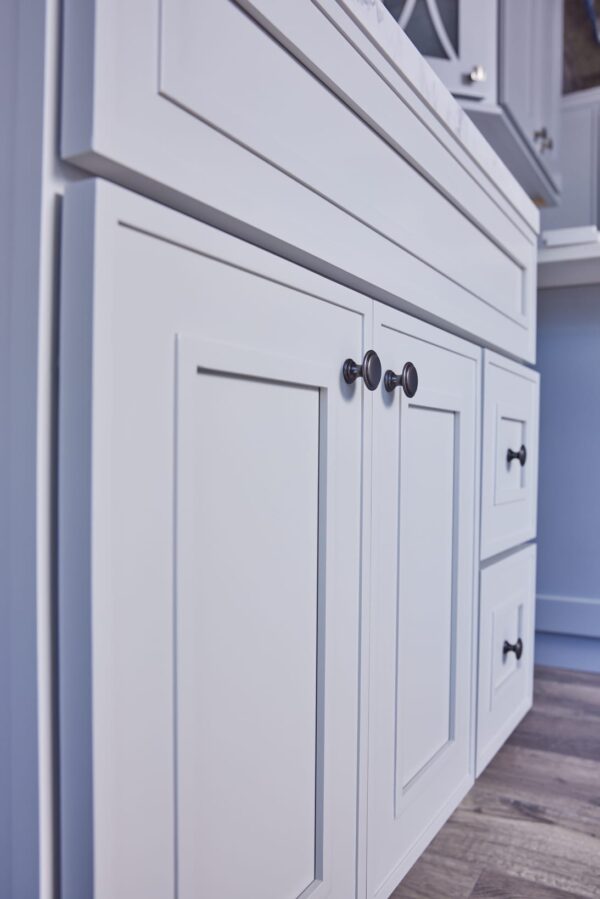 White kitchen cabinets with black knobs on a wooden floor.