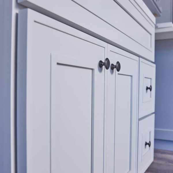 White kitchen cabinets with black knobs on a wooden floor.