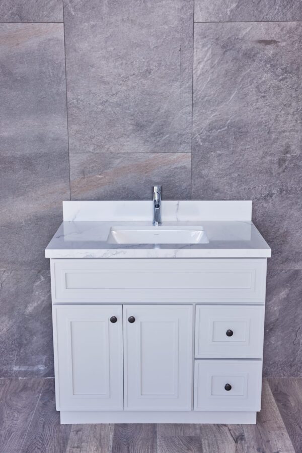 White bathroom vanity with marble countertop against gray stone wall.