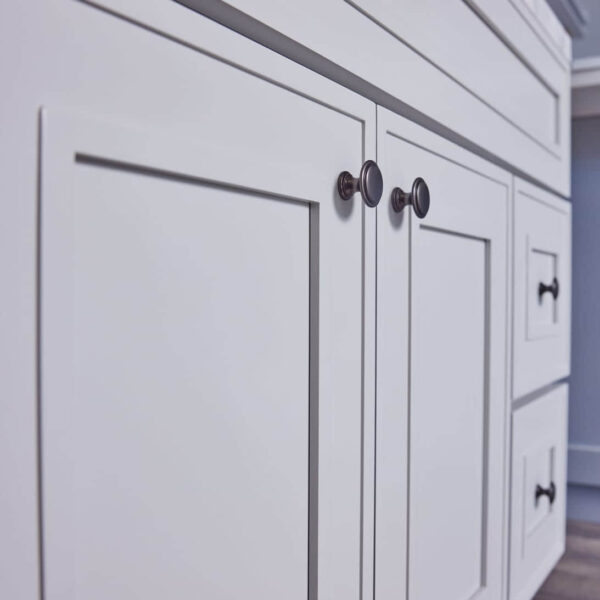 White kitchen cabinets with modern handles on a wooden floor.