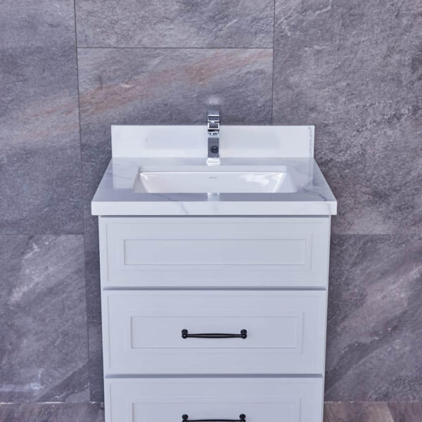 White bathroom vanity with three drawers and a sink, against a gray tiled wall.