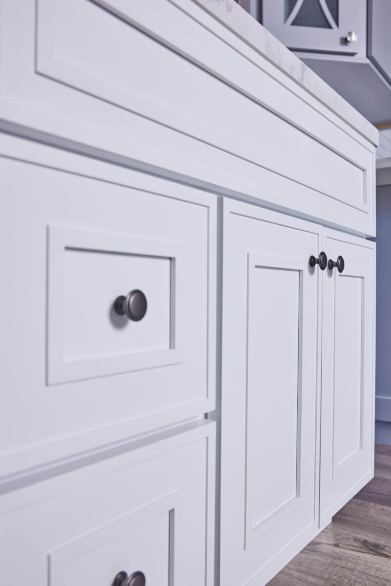 White kitchen cabinets with black knobs and a marble countertop.