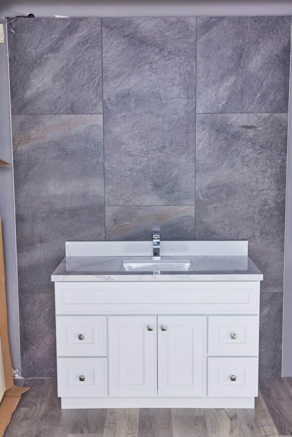 White bathroom vanity with marble countertop against gray tiled wall.