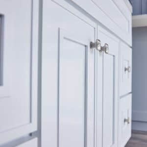White kitchen cabinets with silver handles on a wooden floor.
