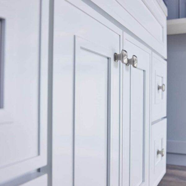 White kitchen cabinets with silver handles on a wooden floor.