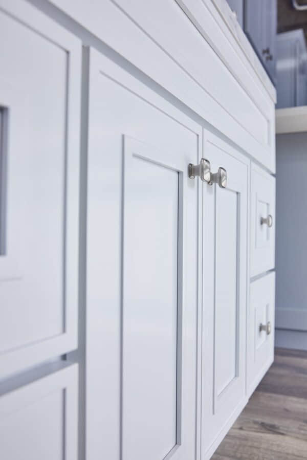 White kitchen cabinets with silver handles on a wooden floor.