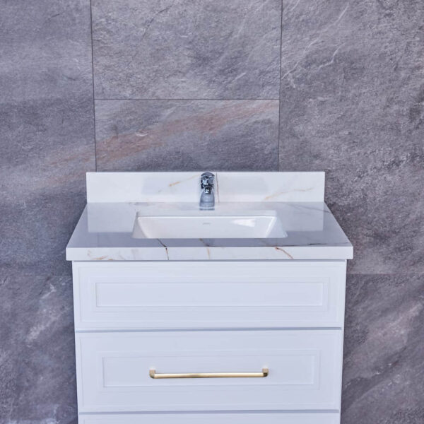 White bathroom vanity with marble countertop and gold handles against gray tile wall.