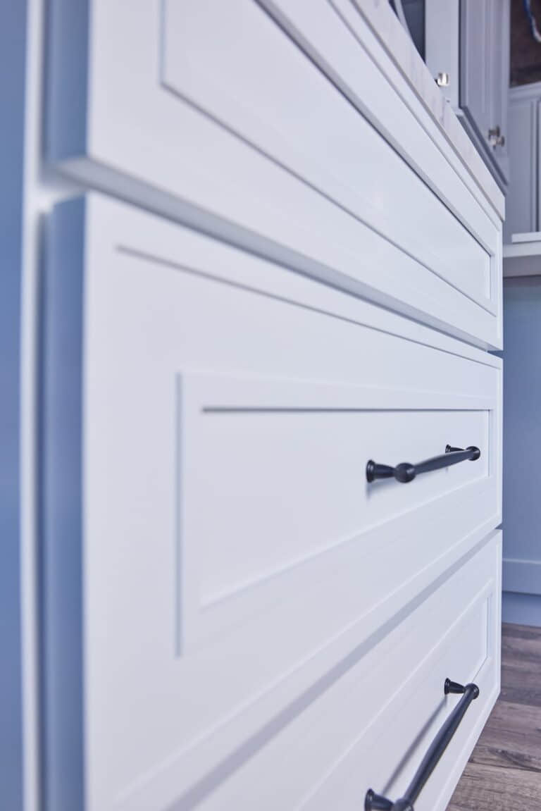Close-up of white kitchen cabinets with black handles.