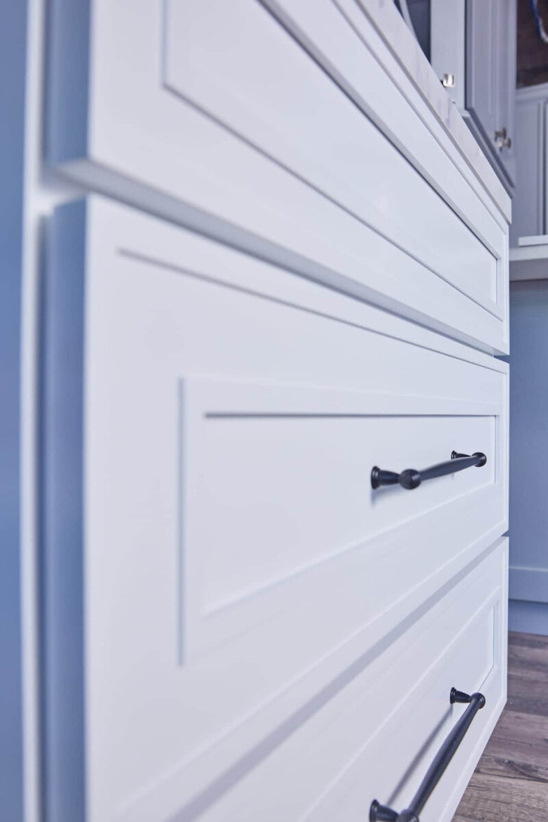 Close-up of white kitchen cabinets with black handles.