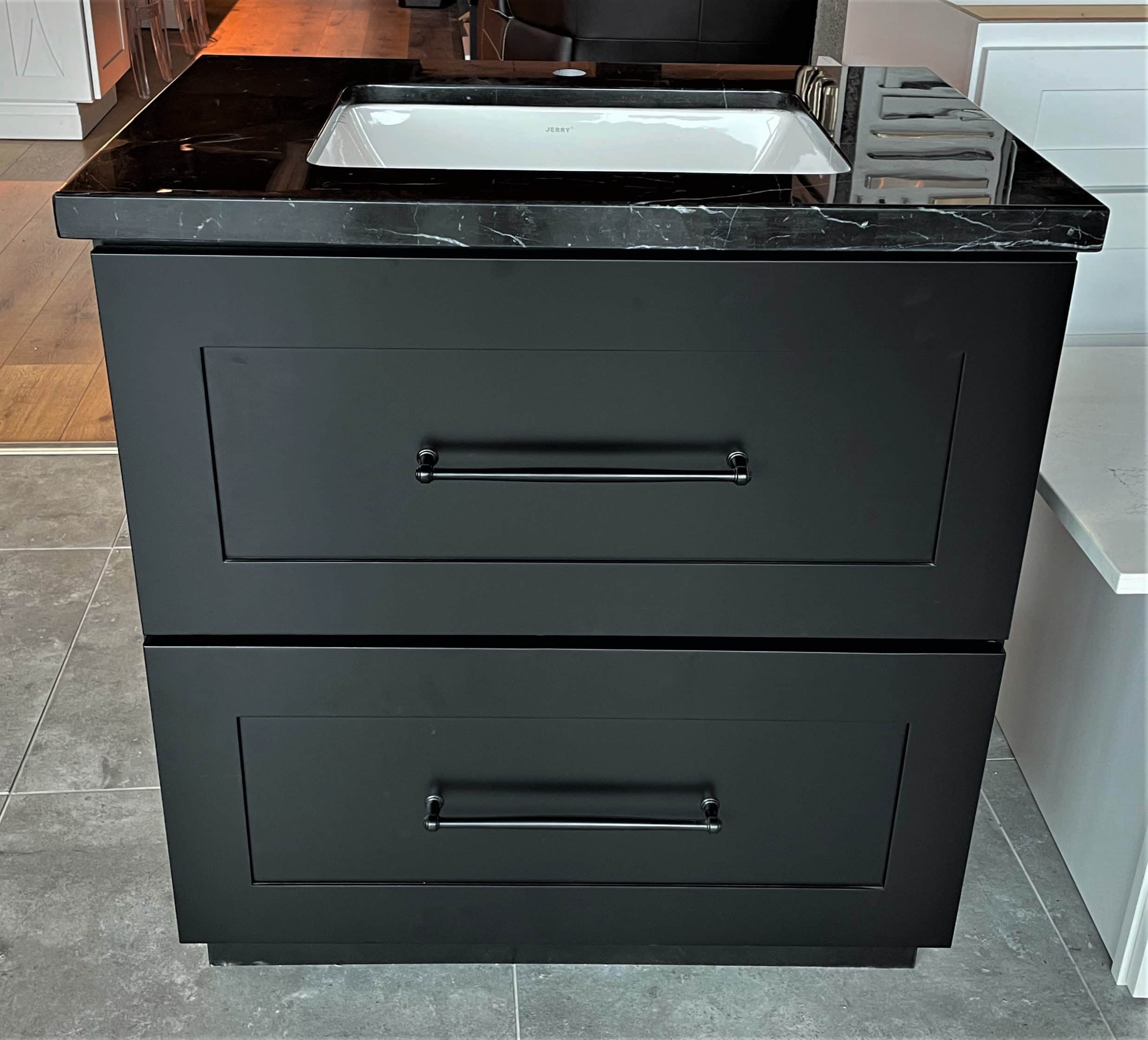 Black freestanding vanity with drawers and marble top in a showroom.