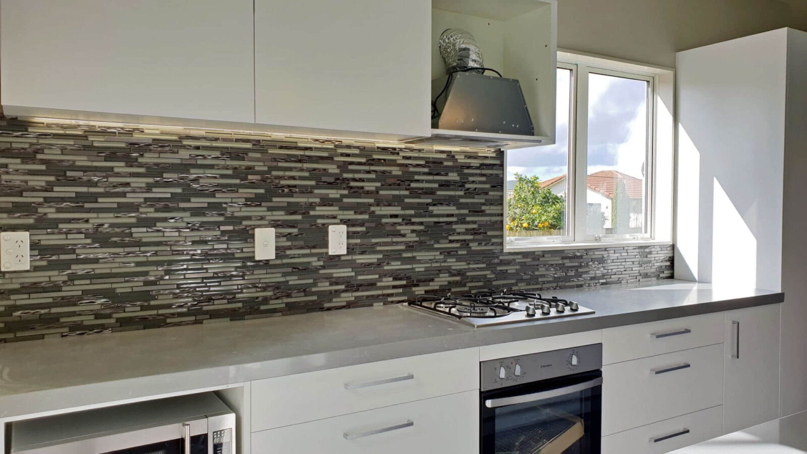 Modern kitchen with gray tile backsplash and stainless steel appliances.
