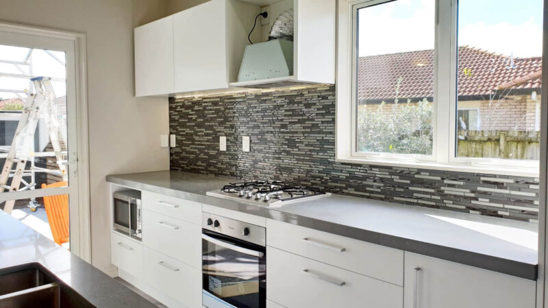 Modern kitchen with gray countertops and mosaic backsplash.
