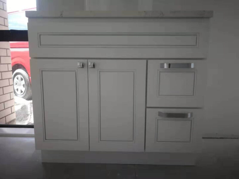 White kitchen cabinet with drawers and doors, against a window.
