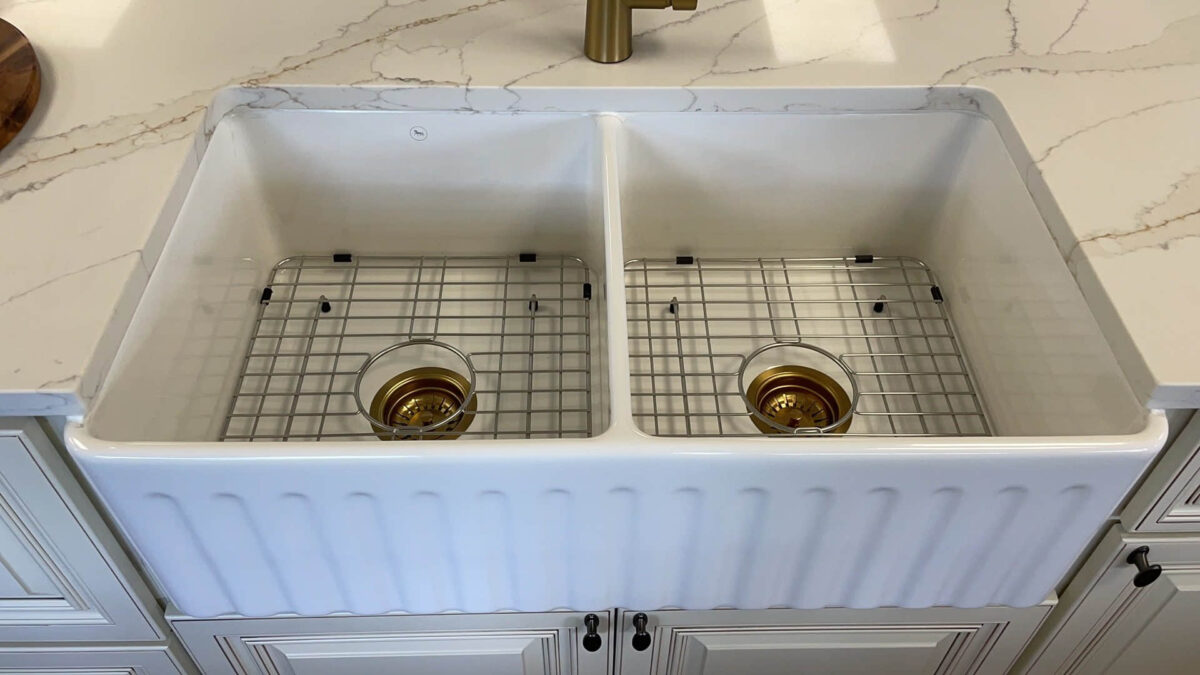 Double farmhouse sink with gold drain covers on marble countertop.
