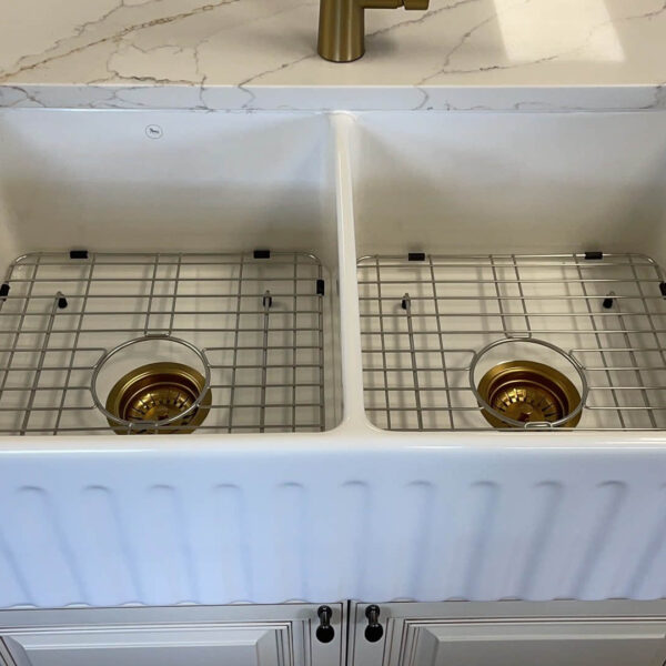 Double farmhouse sink with gold drain covers on marble countertop.