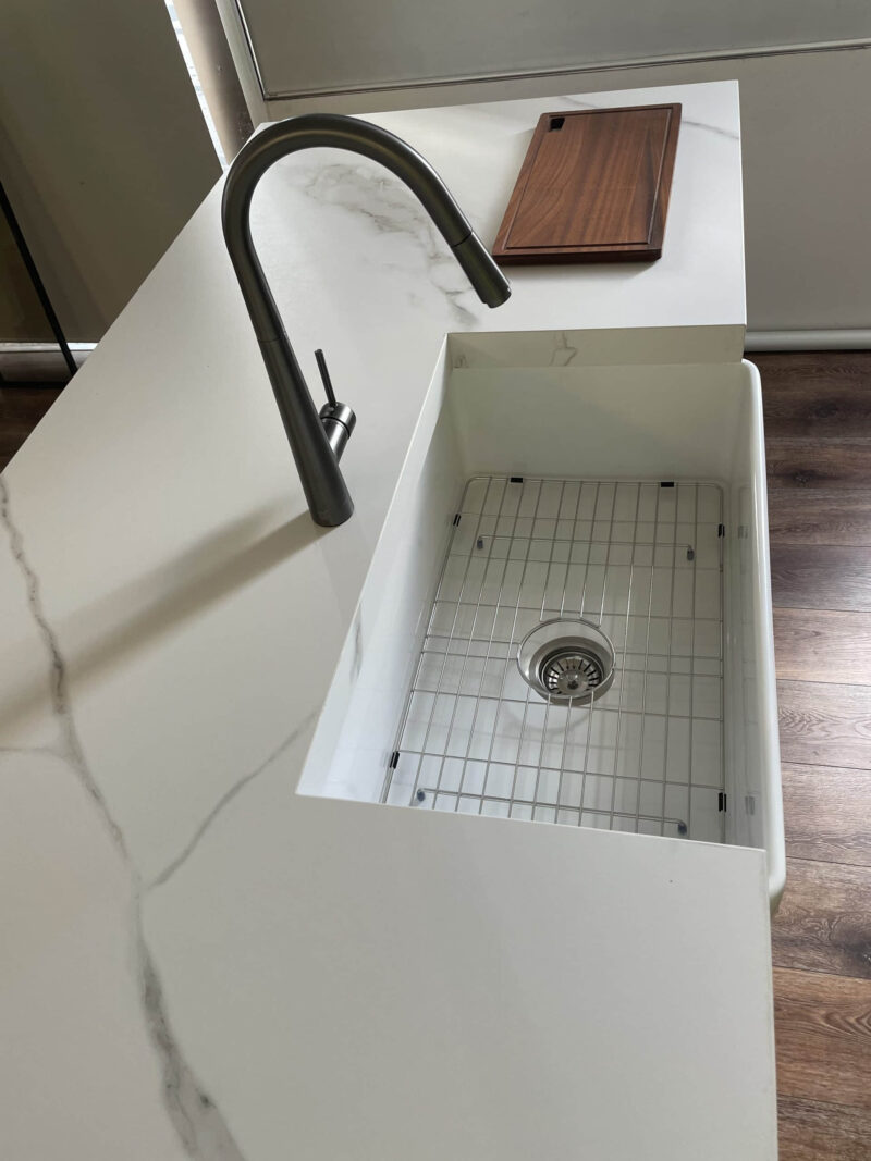 Modern kitchen sink with marble countertop and wooden cutting board.