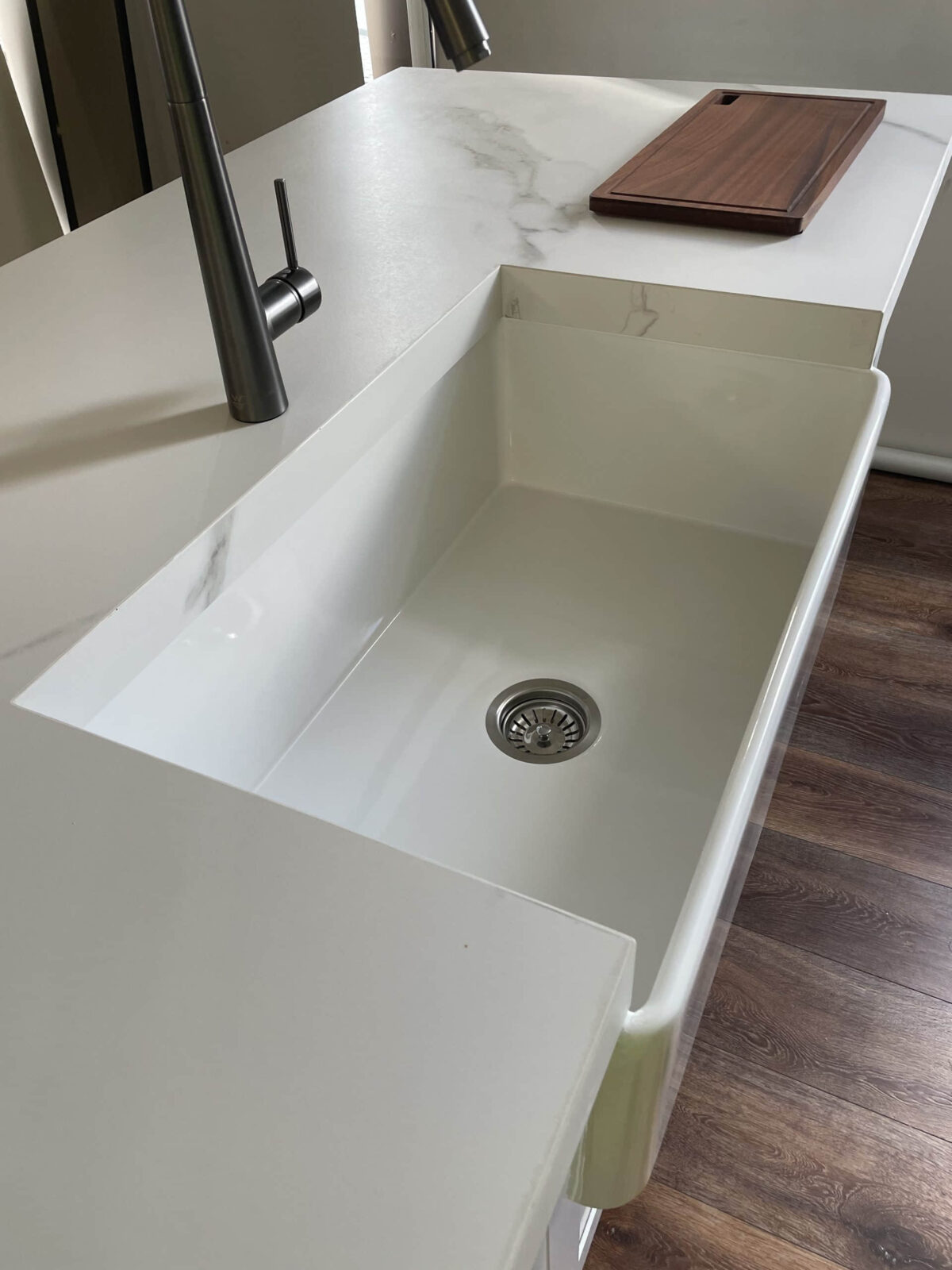 Modern kitchen sink with marble countertop and wooden cutting board.