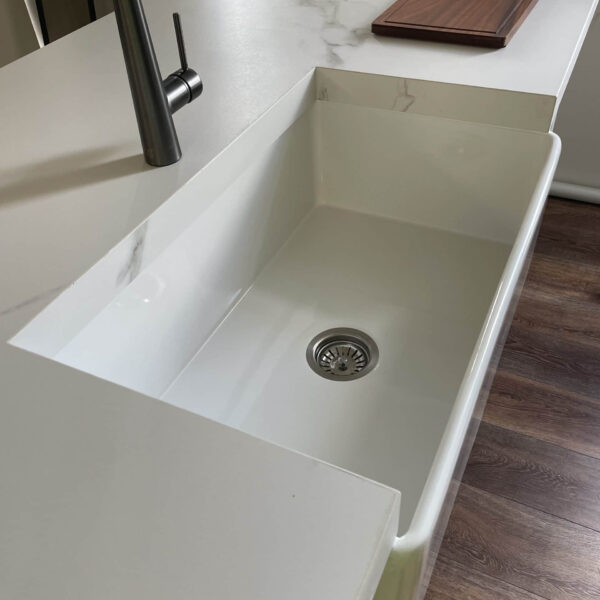 Modern kitchen sink with marble countertop and wooden cutting board.