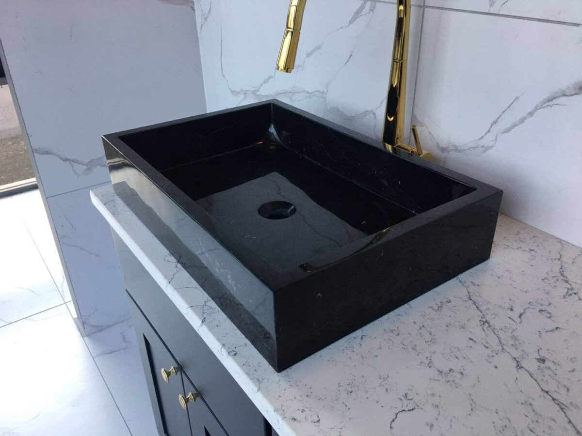 Black marble sink on white marble countertop with gold faucet.